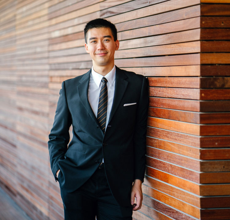 Retrato de un hombre de negocios con traje elegante Hombre joven con traje negro y corbata rayada, apoyado en una pared de madera, sonriendo con confianza
